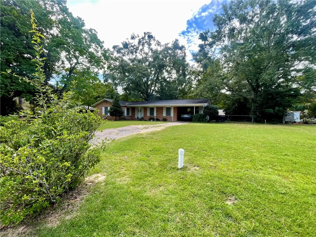 Mature trees frame a classic single-story brick facade fronted by an expansive grassy lawn.