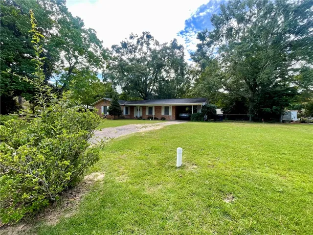 Mature trees frame a classic single-story brick facade fronted by an expansive grassy lawn.