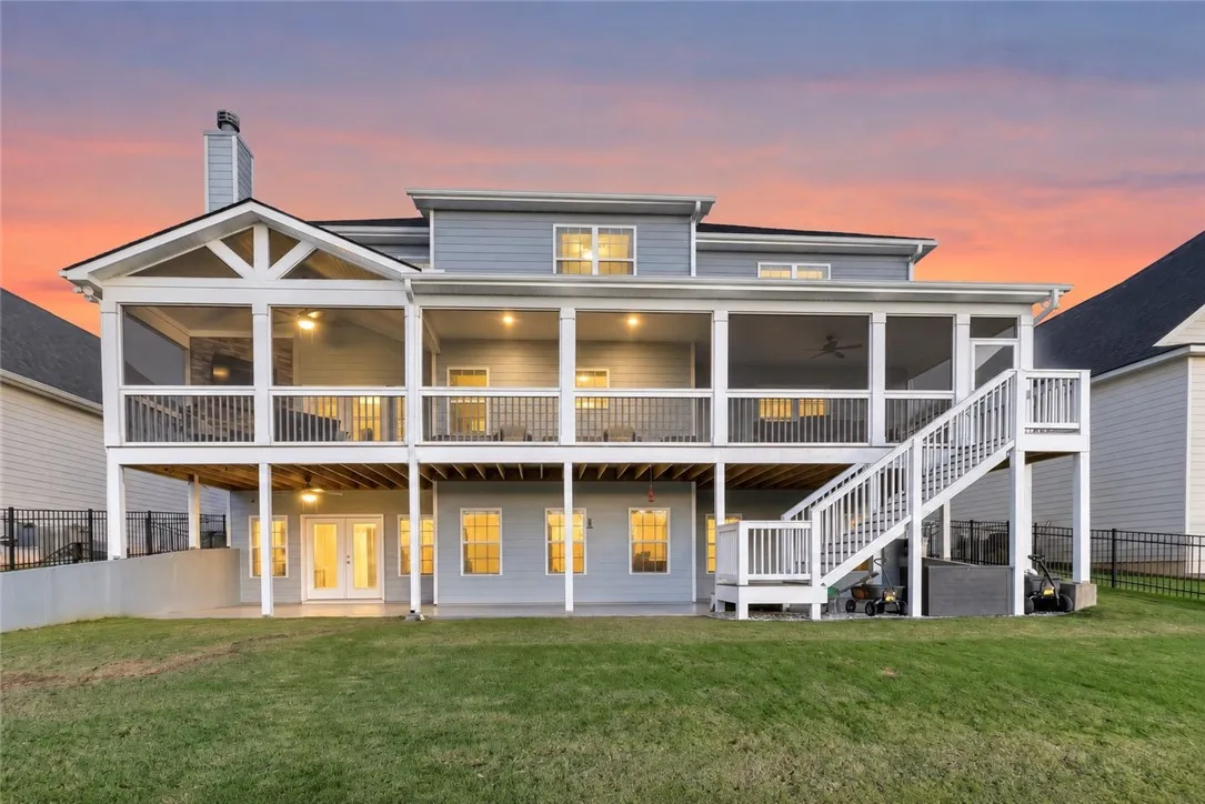 A spacious multi-level deck and covered porch overlook the grassy backyard at dusk.