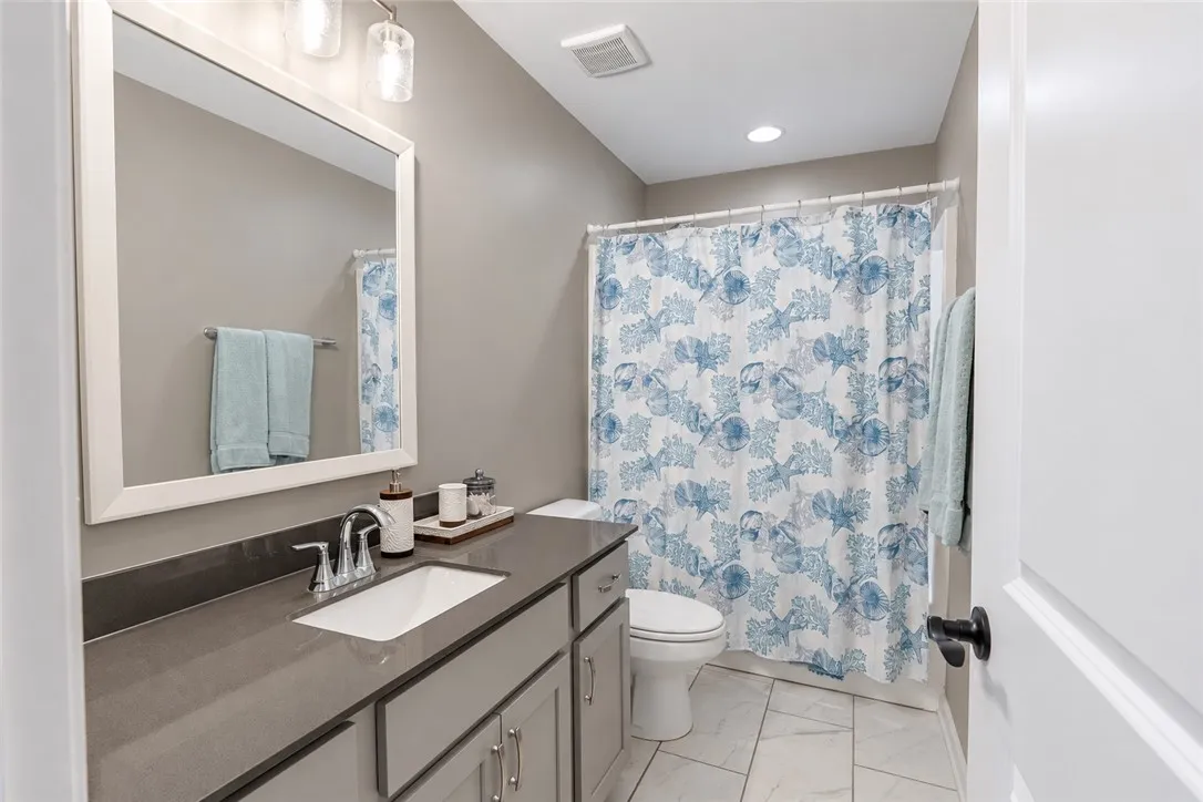 A modern vanity with stone counters complements the clean tile flooring in this bathroom.
