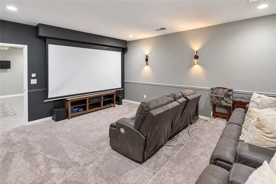 An inviting home theater room features tiered flooring, soft carpeting, and custom wall sconces.