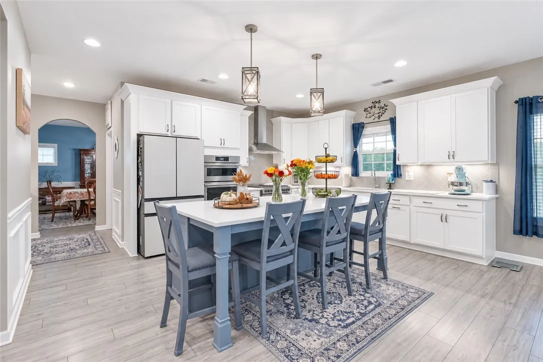 An inviting kitchen features a central island, recessed lighting, and elegant white cabinetry.