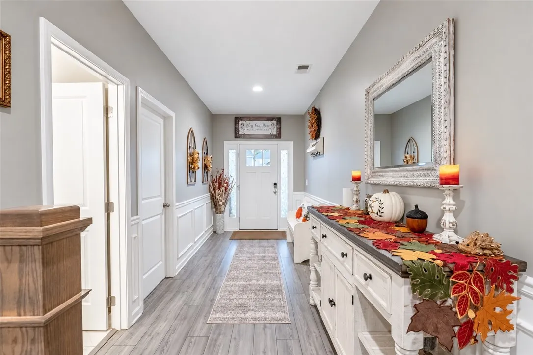 An inviting entrance hallway boasts classic wainscoting and smooth wood-look flooring leading to the front door.