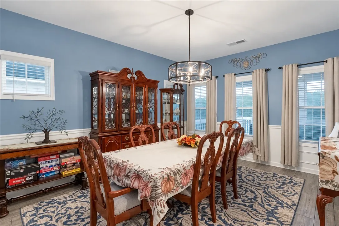 An elegant dining space features rich wood details, wainscoting, and a modern drum chandelier.