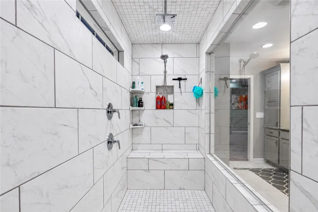 Fine tilework surrounds a spacious walk-in shower featuring a built-in bench and glass enclosure.