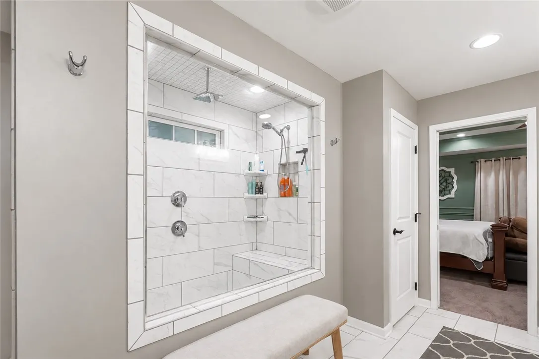Elegant tile work surrounds a glass-enclosed walk-in shower situated adjacent to the bedroom entry.