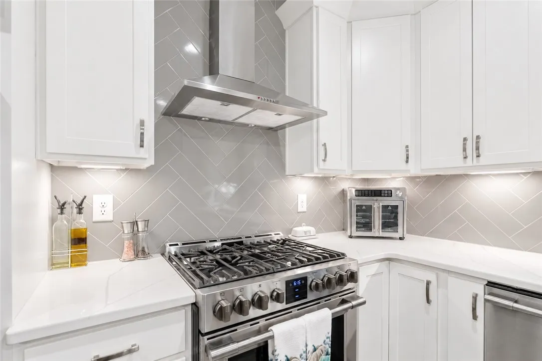 White cabinetry and a glossy herringbone tile backsplash complement the professional-grade stainless steel range.