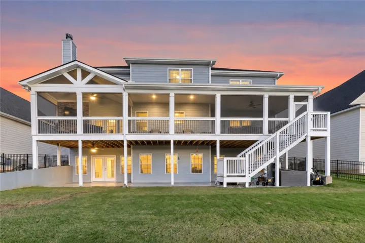 A spacious multi-level deck and covered porch overlook the grassy backyard at dusk.