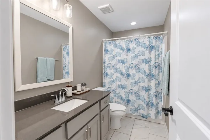 A modern vanity with stone counters complements the clean tile flooring in this bathroom.