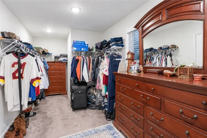 An organized walk-in closet boasts soft neutral carpeting and recessed overhead lighting.
