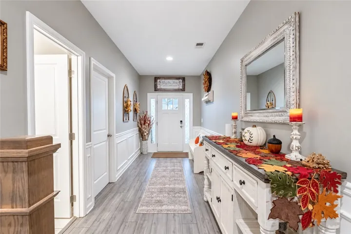 An inviting entrance hallway boasts classic wainscoting and smooth wood-look flooring leading to the front door.