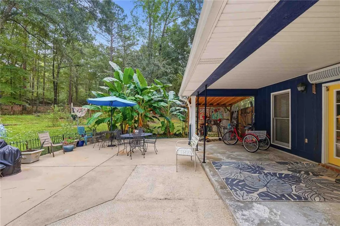 An expansive concrete patio extends from the home toward a lushly wooded backyard border.