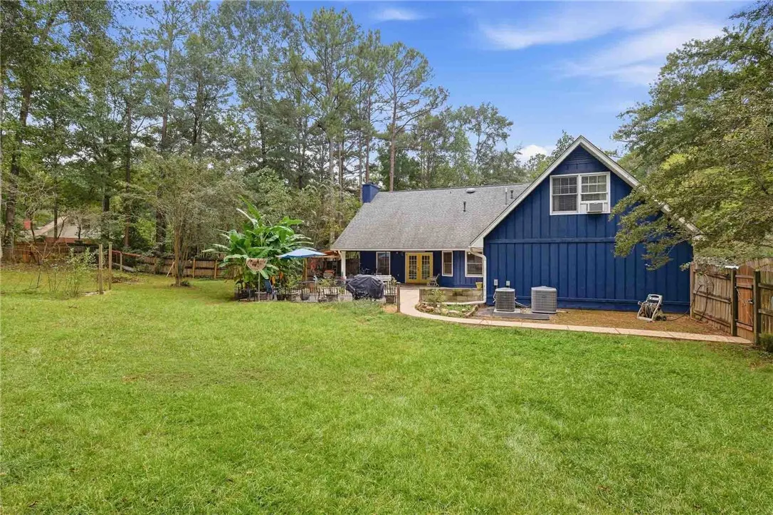 A spacious grassy lawn stretches behind a multi-level home framed by towering mature trees.