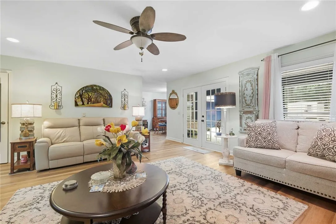 Sunlight streams through French doors into a living space featuring wood floors and recessed lighting.