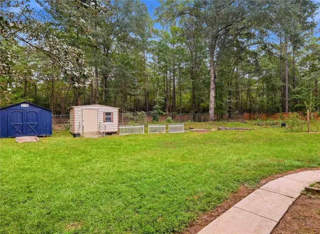 Mature trees frame a grassy lawn featuring convenient storage sheds and a concrete walkway.
