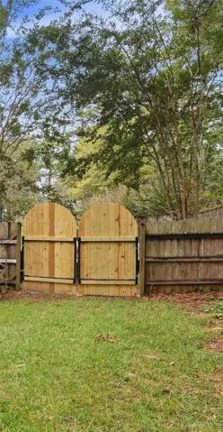 Mature trees shade a grassy lawn enclosed by a wooden privacy fence with double gates.