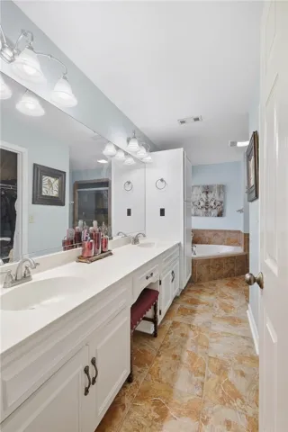 A long vanity with dual sinks anchors this bathroom featuring a corner soaking tub.