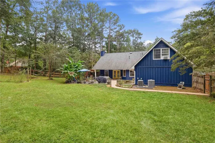 A spacious grassy lawn stretches behind a multi-level home framed by towering mature trees.
