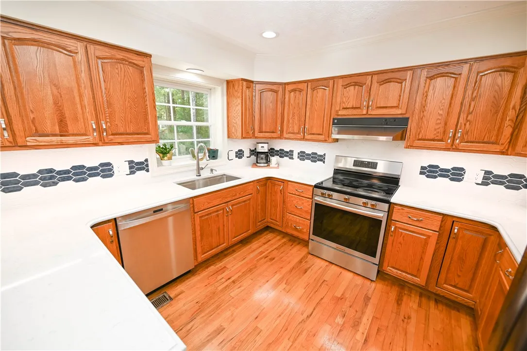 Bright, cheerfully updated kitchen features new SS appliances, quartz countertops, large single-basin SS sink, and custom tile backsplash highlighted by under-cabinet lighting.