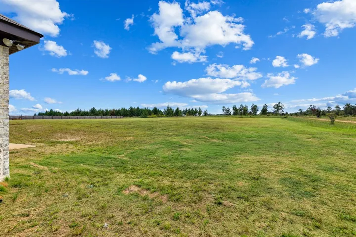 A spacious green lawn stretches out under a clear blue sky bordered by distant trees.