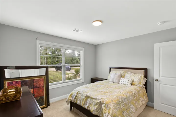 A quiet bedroom features soft wall colors, plush carpeting, and a large window looking outdoors.