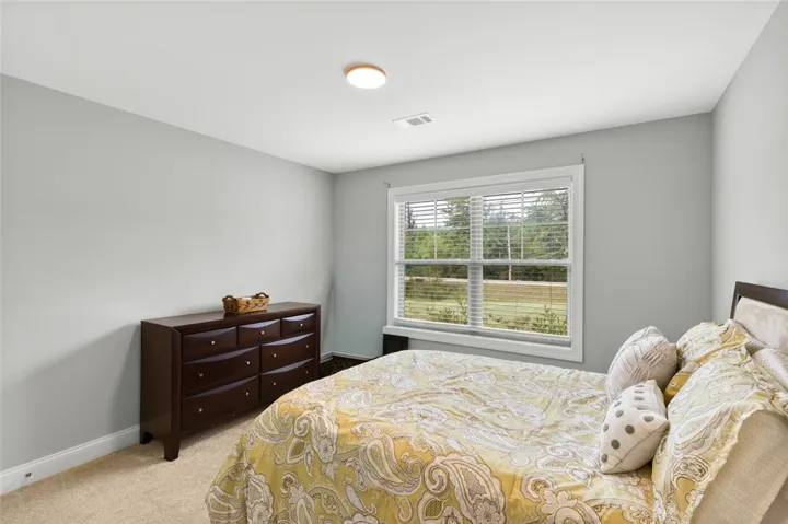 Plush carpeting and a large window framing natural views define this serene bedroom.