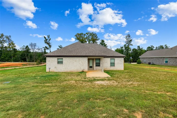 A spacious grassy lawn stretches behind this classic brick home under open blue skies.