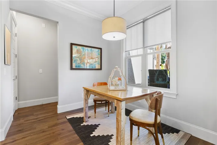 Gleaming hardwood floors and classic crown molding frame a sunlit dining area with tall windows.