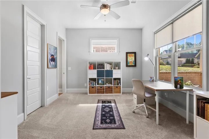 Sunlight streams through large windows into this versatile home office with neutral carpet flooring.