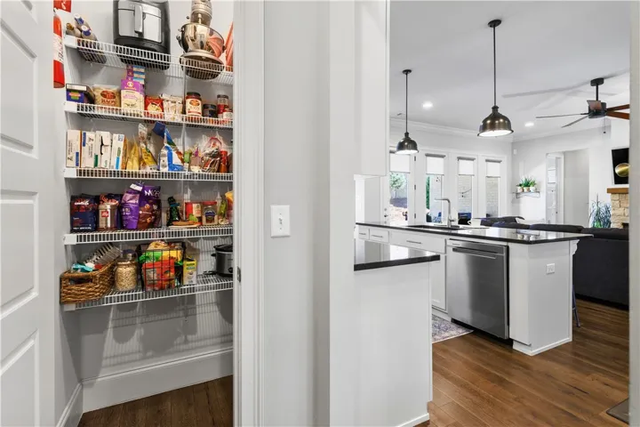 Ample wire shelving fills the dedicated walk-in pantry positioned adjacent to the central kitchen.