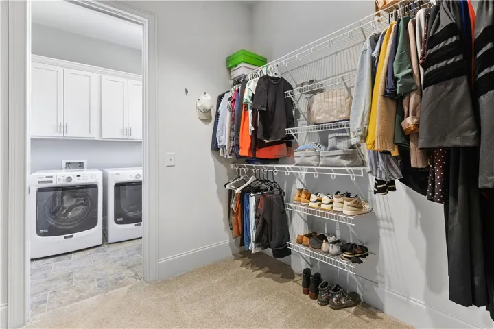 An organized walk-in closet with carpet flooring provides direct access to the adjacent laundry room.