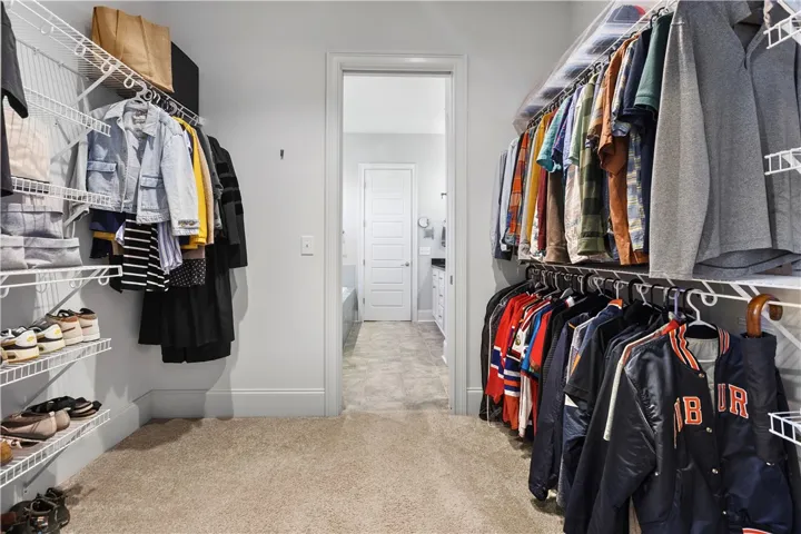 An organized walk-in closet features comfortable carpeting and direct access to the adjacent bathroom.