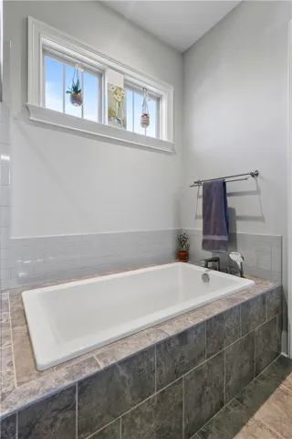 A deep soaking tub is encased in tile under high windows.