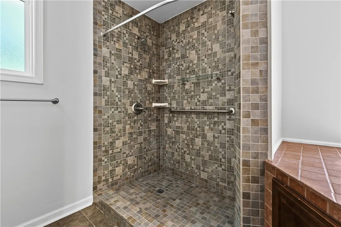 An intricately tiled walk-in shower features built-in shelving, grab bars, and a raised entry curb.