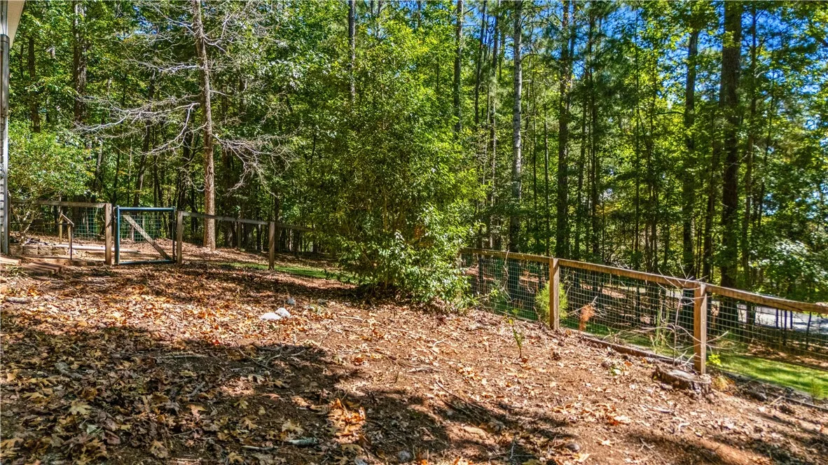 Mature trees frame a gently sloping yard bordered by classic wooden and wire fencing.