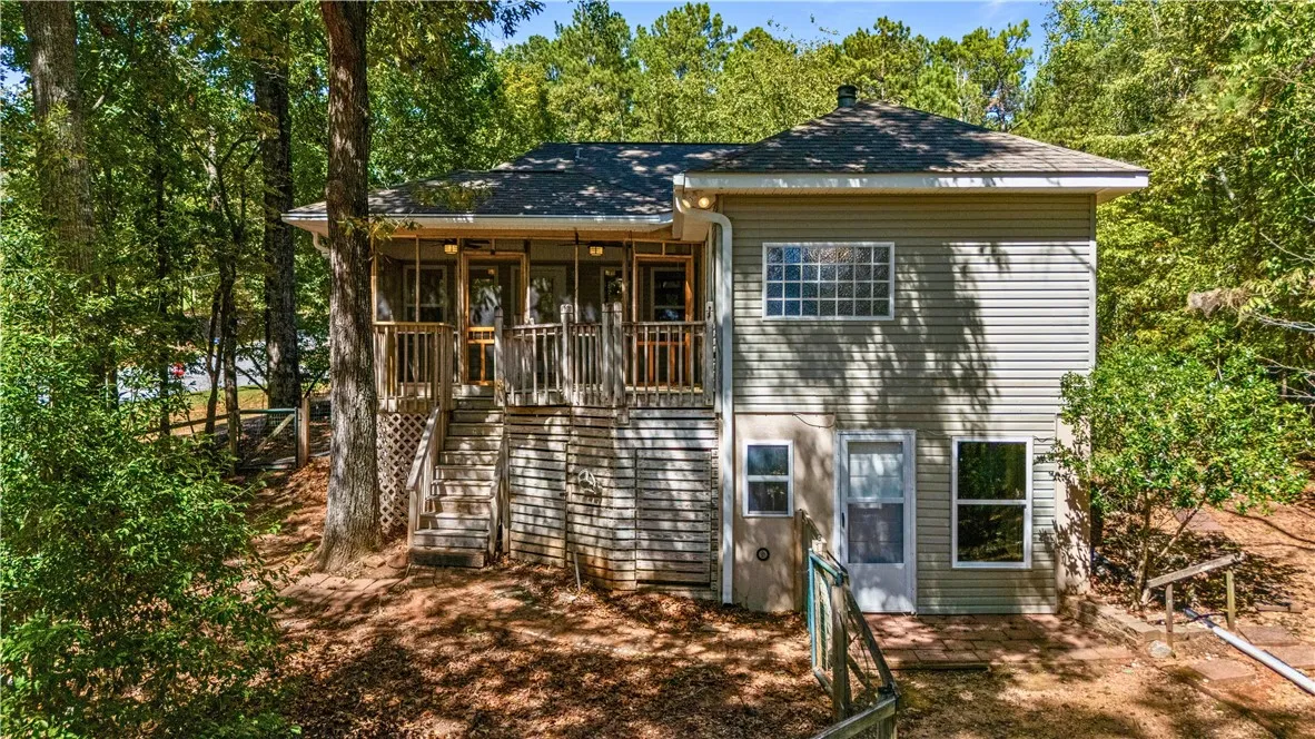 Mature trees frame a multi-level wood-sided home featuring an elevated screened porch. Basement to the right