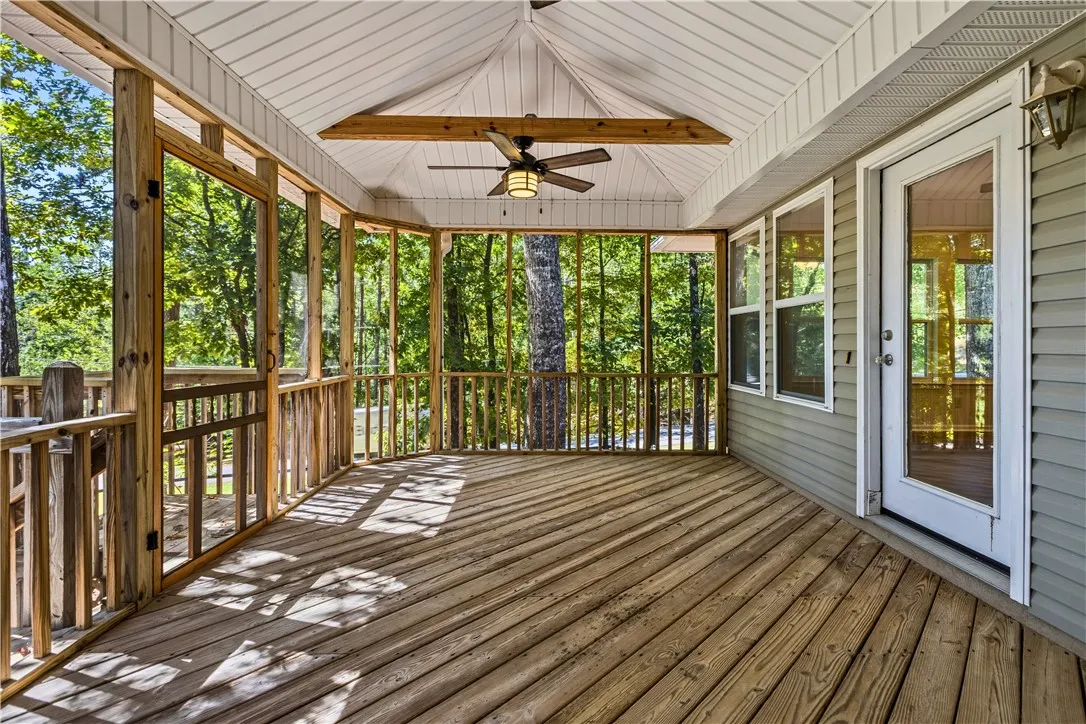 An inviting screened deck features rich wood decking under a vaulted ceiling with rustic beams. New fan/light fixtures