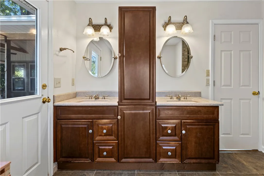 Rich wood cabinetry anchors a functional double vanity flanked by dual entry doors.