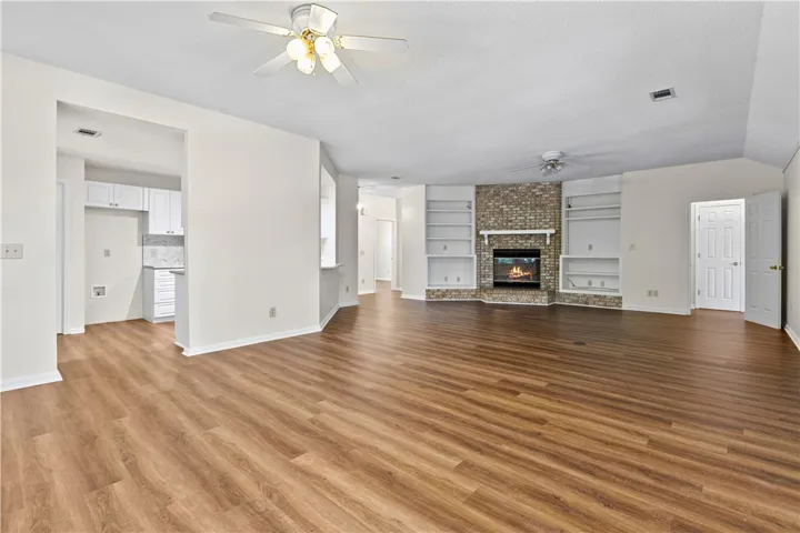 Warm wood-look flooring and a brick fireplace anchor this airy, open-concept living space.