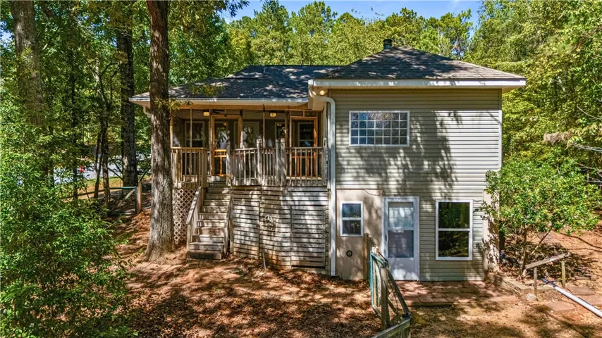 Mature trees frame a multi-level wood-sided home featuring an elevated screened porch. Basement to the right