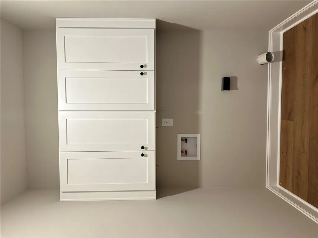 An organized laundry space features shaker cabinetry alongside essential plumbing hookups and durable flooring.