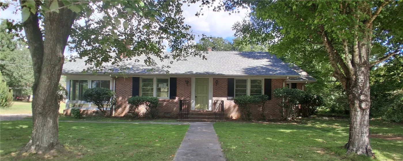 Mature trees shade a classic brick ranch exterior featuring a paved walkway leading to the entry.
