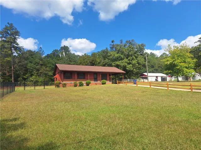 Mature trees frame a classic single-story country home set back on a grassy lawn.