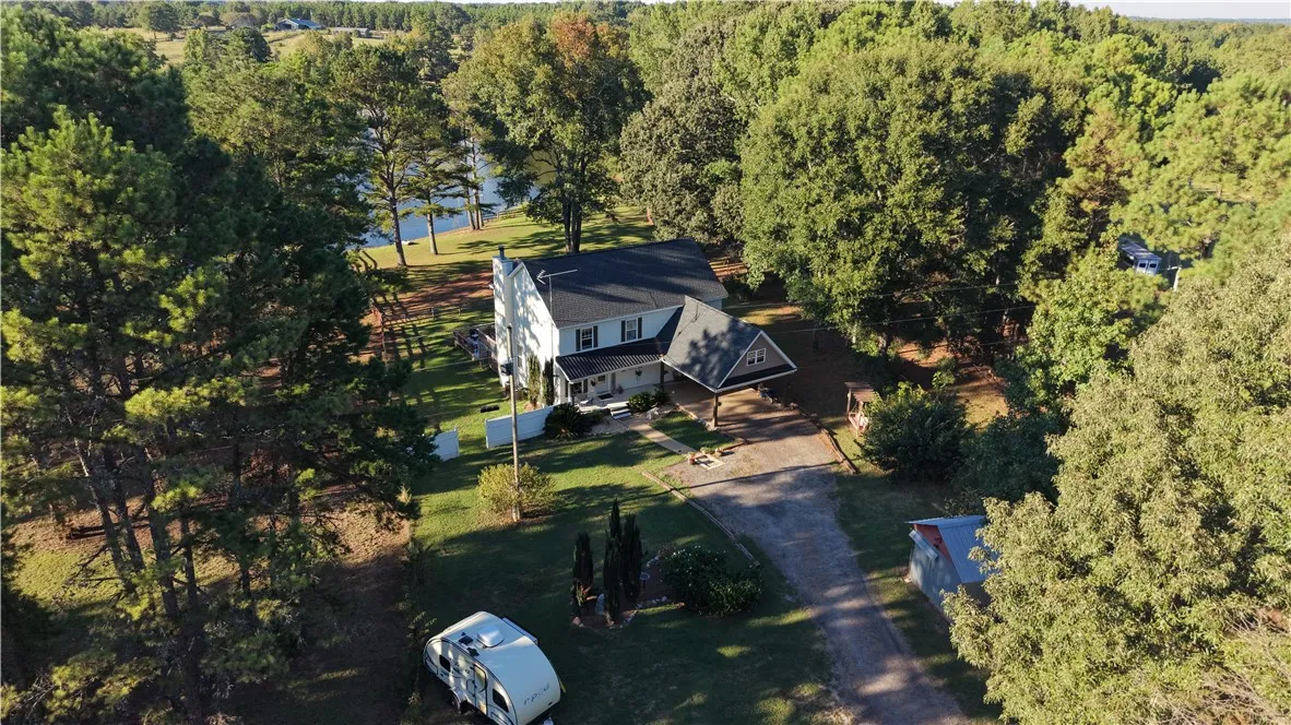 Mature trees frame a two-story country home nestled near a quiet lakefront shoreline.