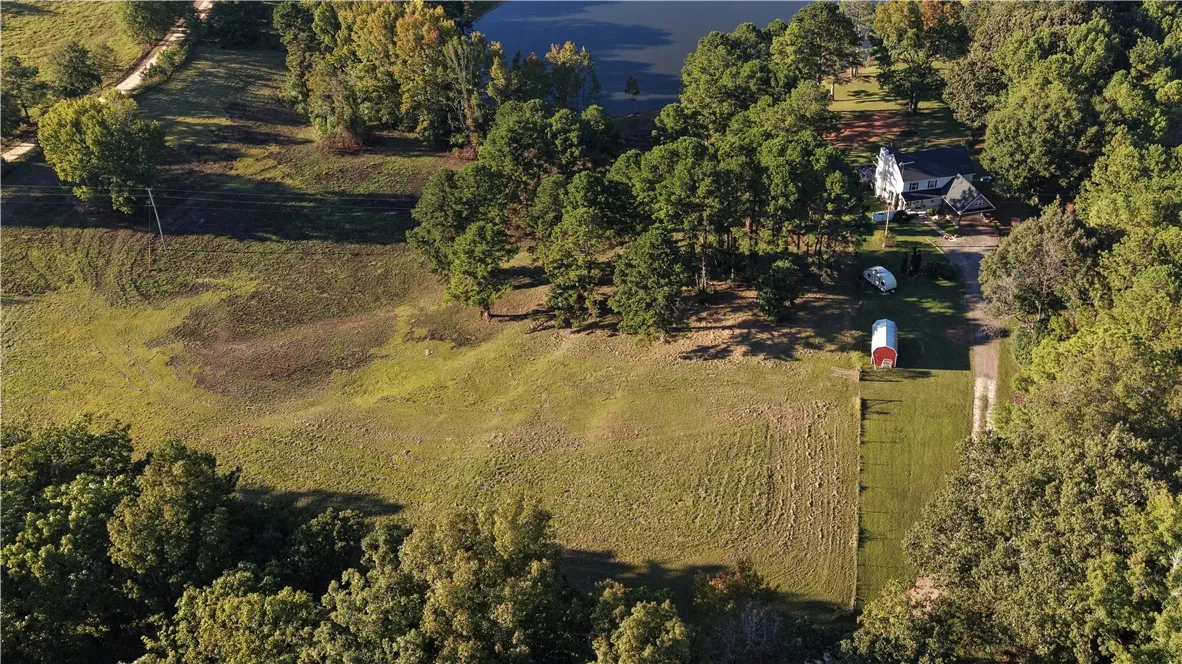 A sweeping aerial view showcases the vast acreage, dense trees, and calm pond of this countryside estate.