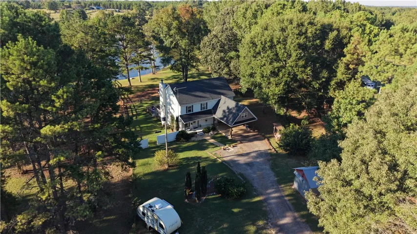 Mature trees frame a two-story country home nestled near a quiet lakefront shoreline.