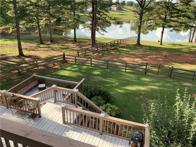 A spacious wooden deck overlooks a fenced yard sloping gently toward a peaceful lakeside setting.