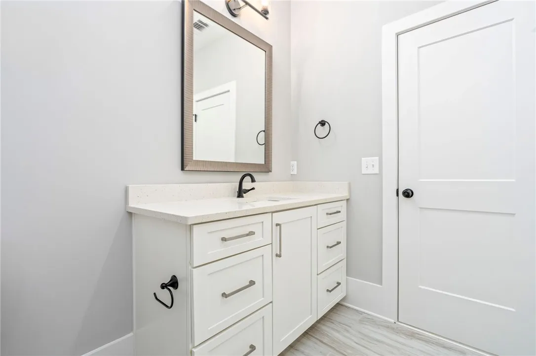 An elegant single vanity with a stone counter sits on wood-look tile flooring.