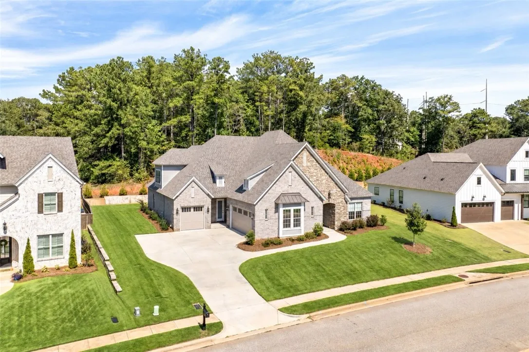 A sweeping concrete driveway leads to this stone-accented suburban home set against a wooded backdrop.