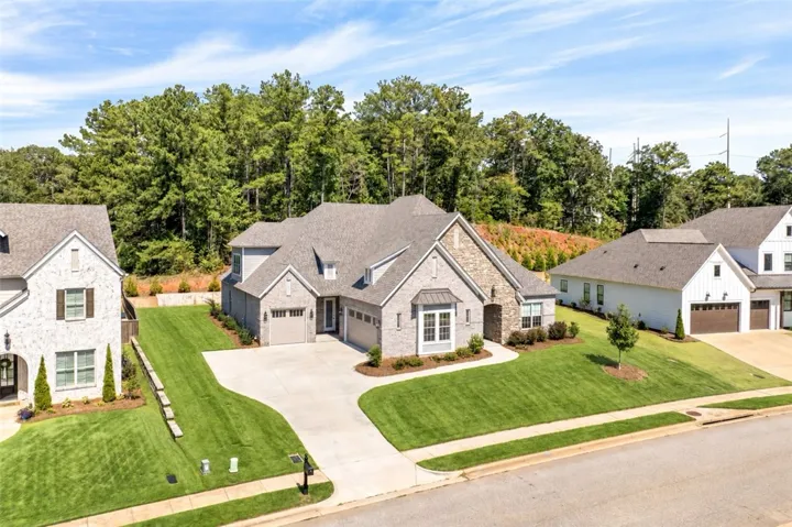 A sweeping concrete driveway leads to this stone-accented suburban home set against a wooded backdrop.